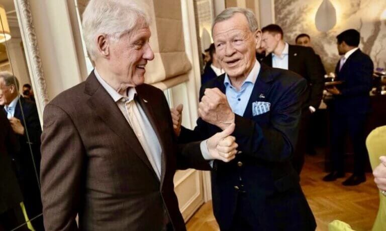 Två äldre kostymklädda män, däribland Anders Wiklöf, ler och skakar hand i ett väl upplyst rum med andra i bakgrunden. En av dem gör en knytnävsgest, vilket speglar kamratskapet bakom murarsonens växande imperium.