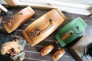 Flera fiskformade lådor i trä och målade av Thord Jannon, med handtag och spännen, är placerade på ett klinkergolv nära ett fönster, tillsammans med andra dekorativa föremål.