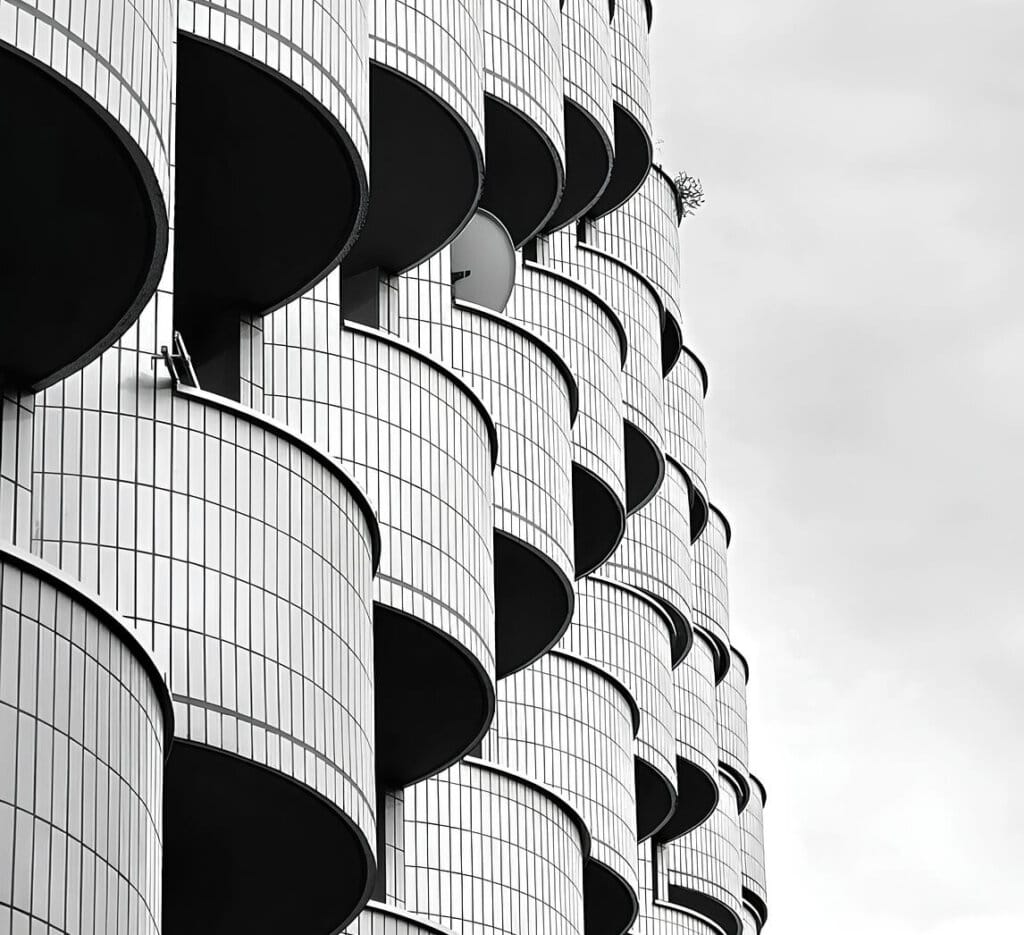 Närbild av en modern byggnadsfasad med upprepade svängda balkonger täckta av vitt kakel, arrangerade i ett förskjutet vertikalt mönster mot en molnig himmel.
