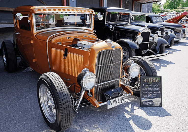 En guldfärgad Ford Coupe 1930 hot rod står parkerad på en bilutställning bredvid andra veteranbilar. På en skylt bredvid står det "Golden A", med information om bilens restaurering och motor.