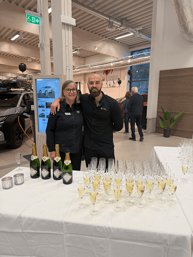 En kvinna och en man i likadana Toyota-arbetsskjortor står bakom ett bord där det står champagneflaskor och glas.