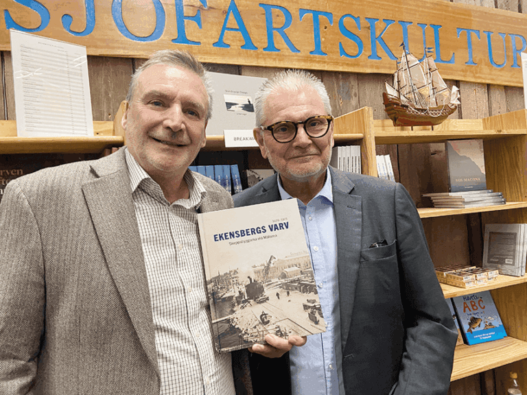 Två män står framför en bokhylla; den ene håller i en bok med titeln ”Ekensbergs Varv”.
